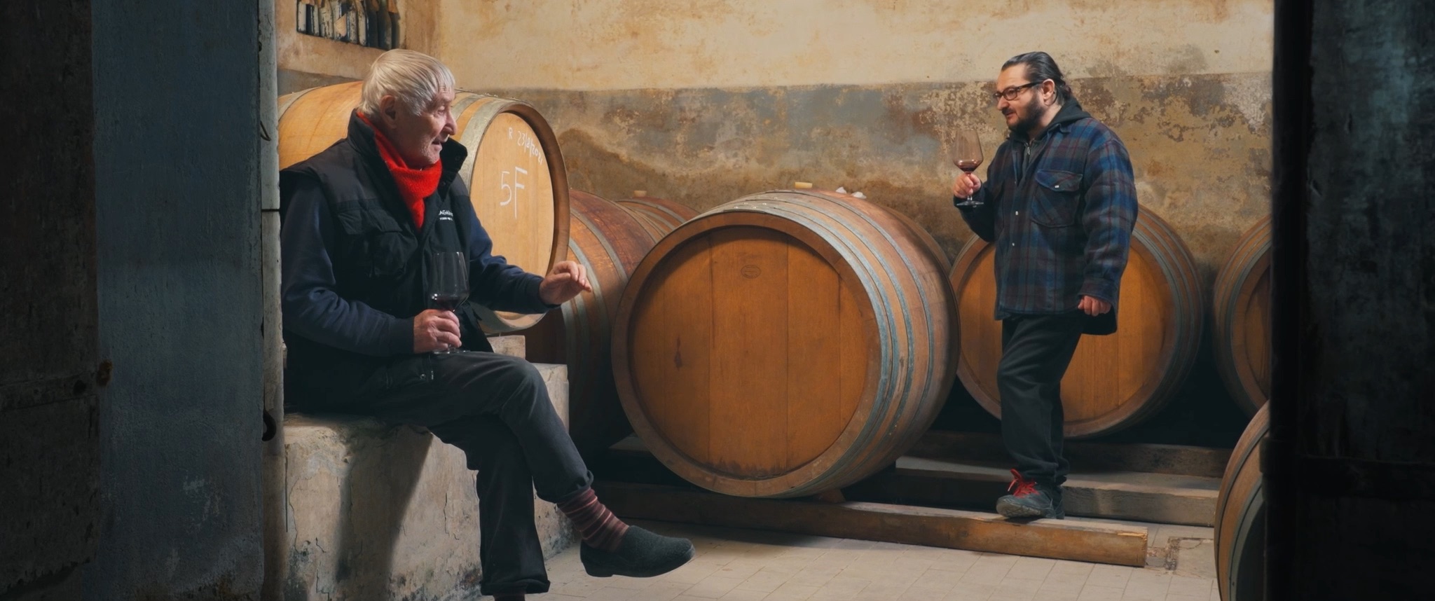 Franco and his son Daniele taste red wine among the oak barrels of their cellar.