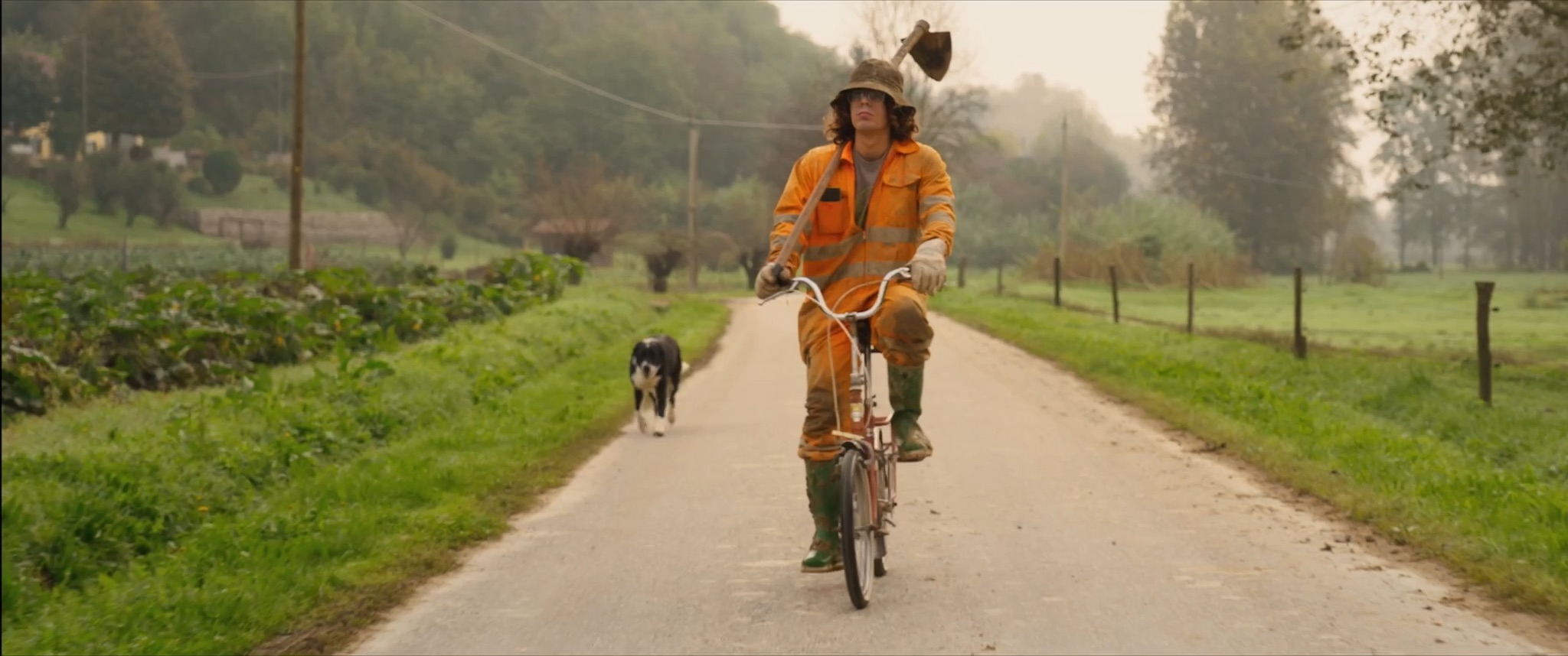 Lorenzo cycles down a misty country road in work overalls, a hoe on his shoulder and his dog trotting behind.
